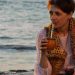 A woman sipping yerba mate while relaxing on a Montevideo beach during sunset.