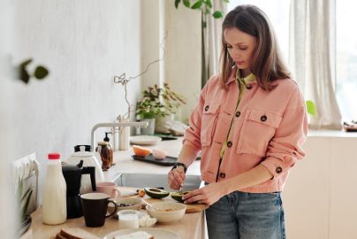 A woman slices an avocado in a bright, modern kitchen with natural light.