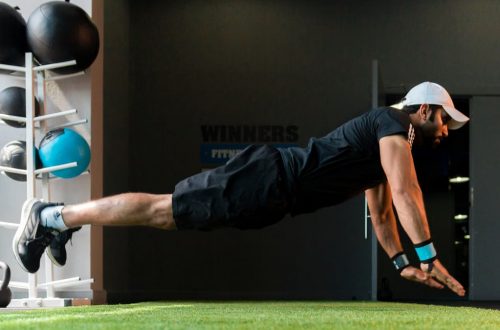 Middle Eastern man doing explosive pushups on gym turf.